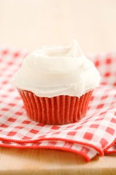 a cupcake with white frosting on a red and white checkered table cloth