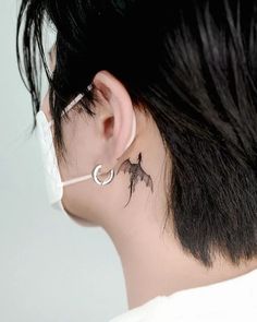 the back of a woman's ear with a small tattoo on her left side