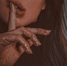 a close up of a person with gold glitter on her face and hand near her mouth