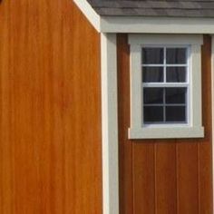 a small wooden shed with a white window and brown shingles on the side of it