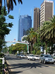 cars are driving down the street in front of tall buildings and palm trees on both sides