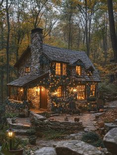 a small stone house with lights on the front and windows, surrounded by greenery