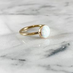 a gold ring with a white opal stone on the front and side, sitting on a marble surface