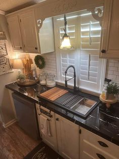 a kitchen with white cabinets and black counter tops, along with a sink that has a wooden cutting board on it