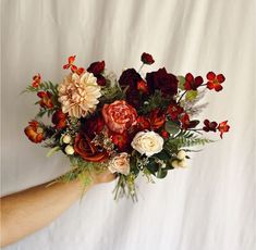 a person holding a bouquet of flowers in their hand on a white background with red and orange colors