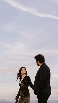 a man and woman standing next to each other on top of a hill holding hands