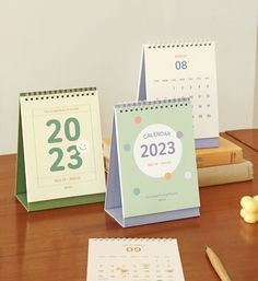 three calendars sitting on top of a wooden table next to books and pencils