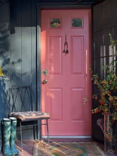 a bright pink door is in front of a black house with an iron bench and side table