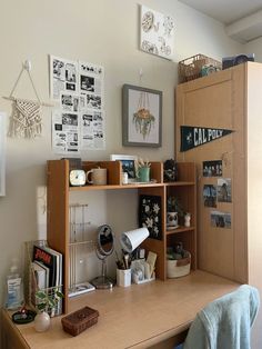 a wooden desk topped with lots of clutter next to a wall covered in pictures