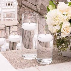 white flowers and candles sit in vases on a table