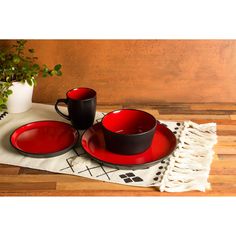 two red cups and saucers sitting on top of a place mat next to a potted plant