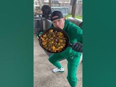 a man in green sweats holding a pan filled with food on top of his chest