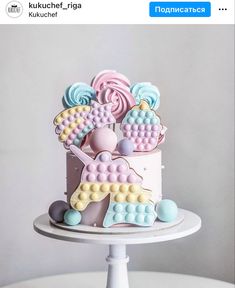 a birthday cake decorated with pastel colors and candies is on a white pedestal