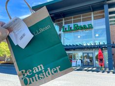 a person holding up a paper bag in front of a building that says bean outsider