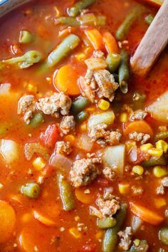 a bowl filled with soup and vegetables next to a wooden spoon