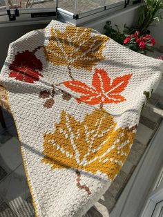 a crocheted blanket on a window sill in front of a potted plant