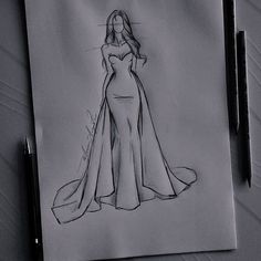 a drawing of a woman in a long dress on a piece of paper next to a pen