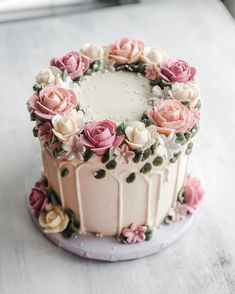 a cake decorated with pink and white flowers on a plate, sitting on a table