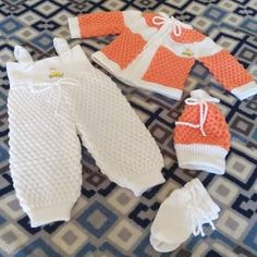 three knitted baby clothes and booties laying on a rug