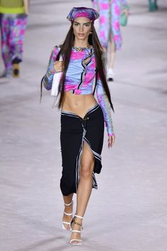 a model walks down the runway in a colorful top and skirt with high slits