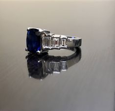 DeKara Designs Classic Metal- 90% Platinum, 10% Iridium. Stones- 1 Cushion Cut Ceylon Blue Sapphire 2.92 Carats. 6 Square Baguette Diamonds, F-G Color VS1 Clarity, 0.94 Carats. A beautiful dark blue Cushion Cut 2.92 Carat Ceylon blue sapphire and diamond platinum ring that is inspired by the Roaring 20's. The ring is true to its Art Deco look with the 3 accenting rectangle baguettes that are channel set with g color and vs1 in clarity totaling to .94 carats. The sapphire is set with four prongs Gia Certified Baguette Cut Sapphire Ring, Modern Sapphire Rings Gia Certified, Gia Certified Timeless Blue Ring, Blue Cushion Cut Ring With Polished Finish, Blue Diamond Platinum Ring With Polished Finish, Blue Platinum Diamond Ring With Polished Finish, Gia Certified Blue Baguette Cut Ring, Blue Gia Certified Baguette Cut Ring, Blue Sapphire Ring With Emerald Cut And Polished Finish