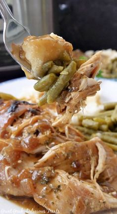 a fork full of food on top of a white plate with green beans and mashed potatoes