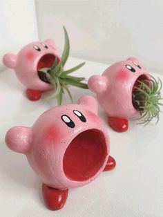 three pink plastic toys with faces on them and one has grass growing out of its mouth