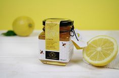 a jar of honey sitting next to an apple and lemon slice on a white table