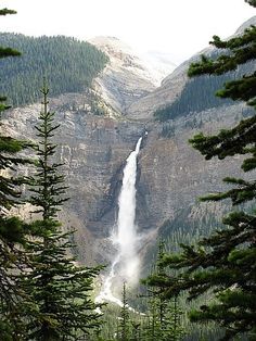 there is a waterfall in the middle of some trees and mountain side area with snow on it