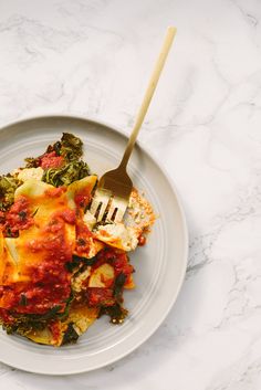 a white plate topped with lasagna covered in sauce and spinach next to a fork