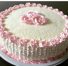 a white cake with pink frosting and roses on the top is sitting on a plate