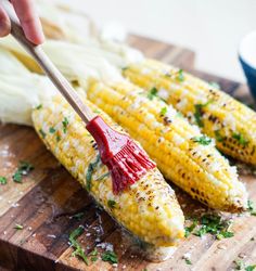 someone is holding a brush over corn on the cob with parmesan cheese