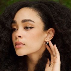 a close up of a person with curly hair wearing ear rings and holding her hand near her ear