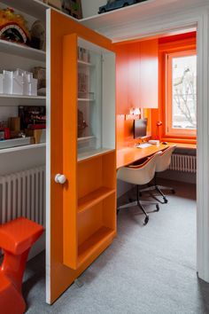 an orange and white room with a desk and chair next to the open bookcase