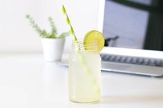 a glass with a lime slice and a straw next to a laptop on a desk