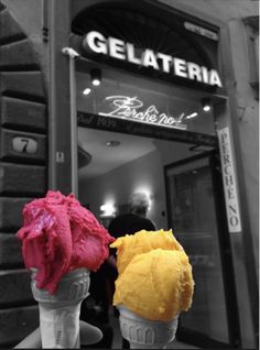 two ice cream cones with yellow and pink toppings in front of a gelateria store