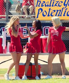 three girls in red cheerleader outfits on the sidelines at a football game, with one holding her fist up