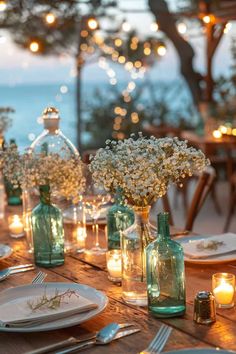 the table is set for dinner with candles and flowers in glass vases on it