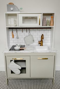 a kitchen with white cabinets and black and white tile flooring, gold handles on the sink