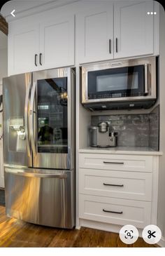 a stainless steel refrigerator and microwave in a kitchen with white cabinets, wood floors and hardwood flooring