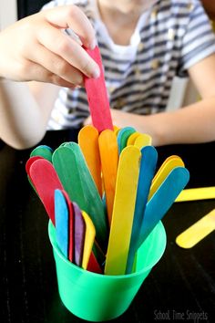 a child is sitting at a table and playing with popsicle sticks in a cup