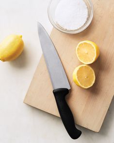 a cutting board with two lemons and a knife next to some salt on it