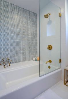 a white bath tub sitting next to a shower with a glass door and gold fixtures