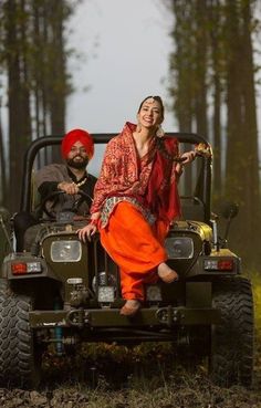 a man and woman sitting on top of a jeep in the middle of a forest