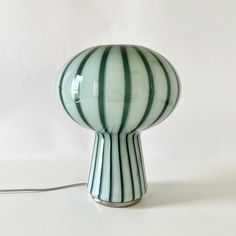 a green and white striped lamp sitting on top of a table next to a cord