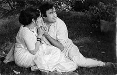 a man and woman sitting on the ground in front of some trees, one is touching her ear