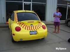 a woman standing next to a yellow car with a baseball painted on the front and side