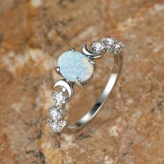 a white opal and diamond ring sitting on top of a rock