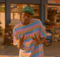 a young man wearing a colorful shirt and green hat standing in front of a store