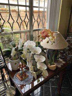 there are many flowers on the table by the window in the room with the lamp